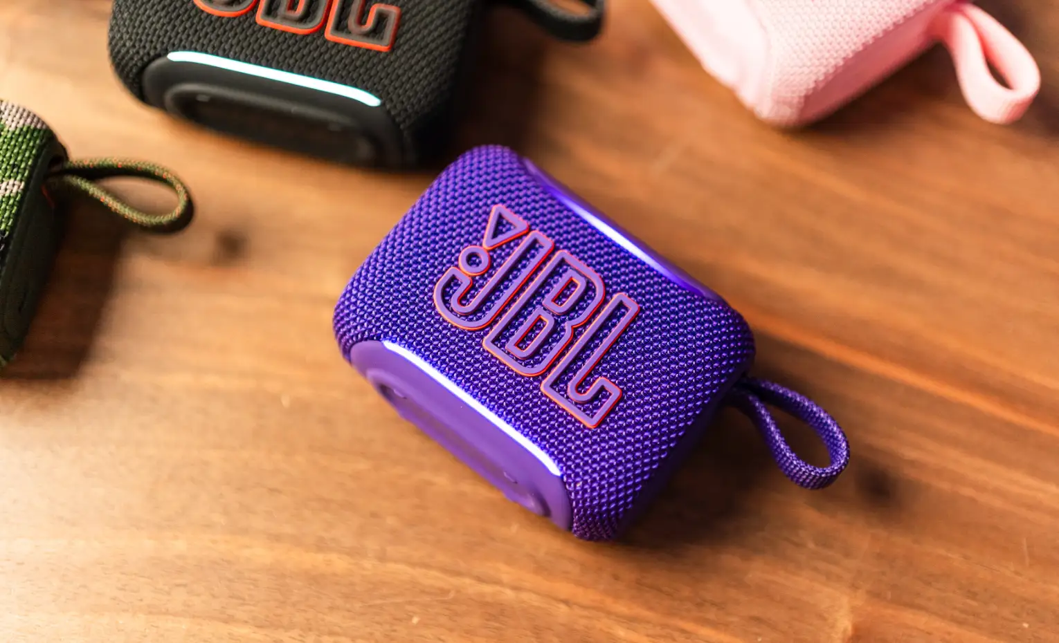 یک اسپیکر بزرگ یا دو کوچک، کدام را بخریم؟ (مهر 1405) اسپیکر بنفش JBL Go با بند حلقهای روی میز چوبی