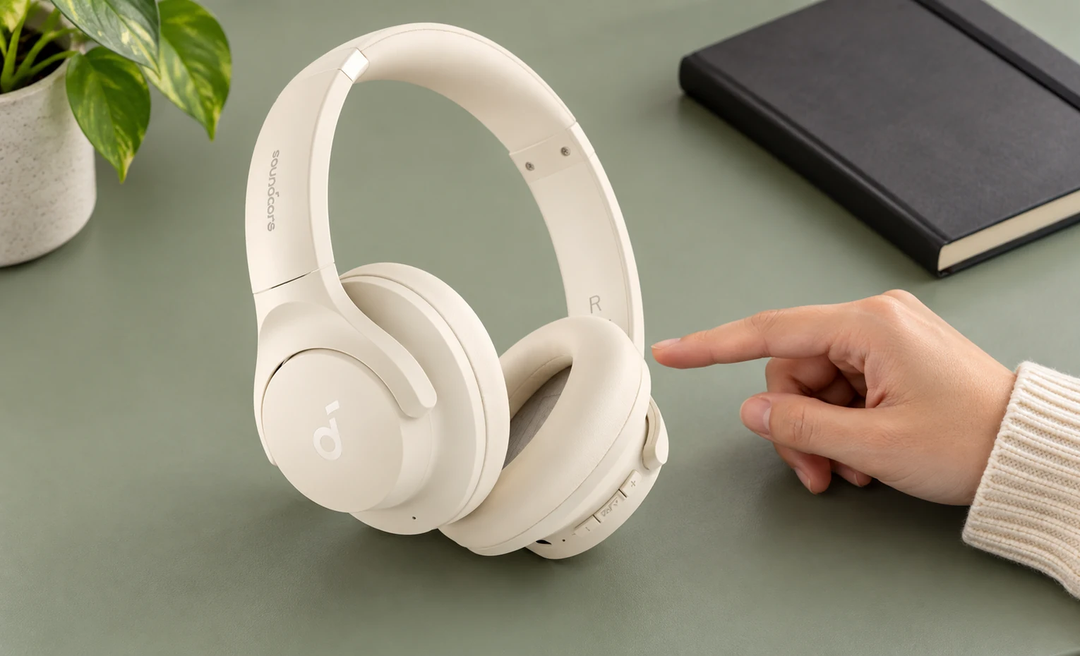 زرد شدن هدفون سفید؛ قبل از خرید چه بدانیم؟ کاربر در حال اشاره به هدفون کرمرنگ Soundcore روی میز