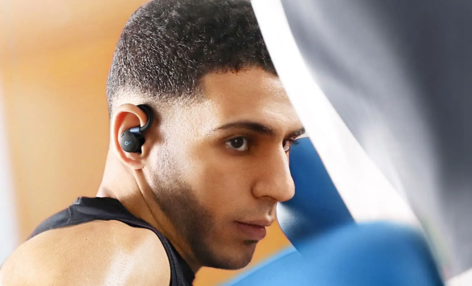 هندزفری انکر Soundcore Sport X20، بررسی برای ورزش و دویدن ورزشکار با هندزفری مشکی Sport X20 در گوش کنار کیسه بوکس