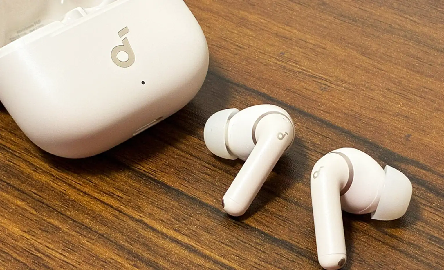 هندزفری انکر P42i؛ حذف نویز با دو حالت متفاوت هندزفری سفید Soundcore P42i کنار کیس بسته روی میز چوبی